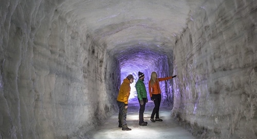 Three persons looking at an ice wall inside the Ice Tunnel