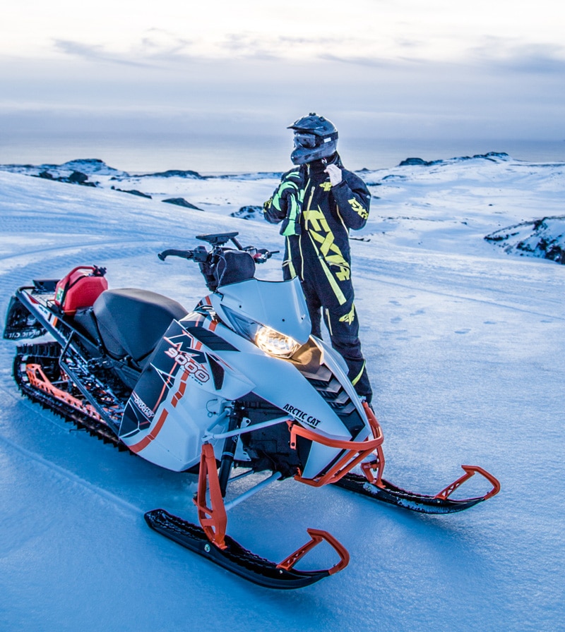 Person in snowmobile gear standing next to a snowmobile on a glacier