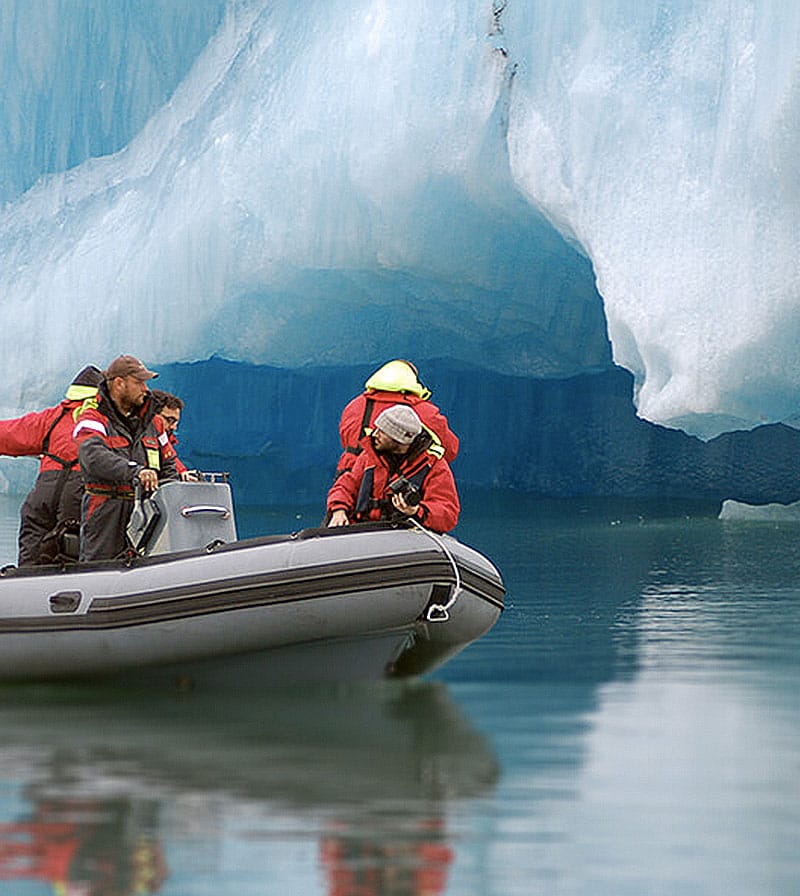Three guys on a Zodiac boat next to an iceberg