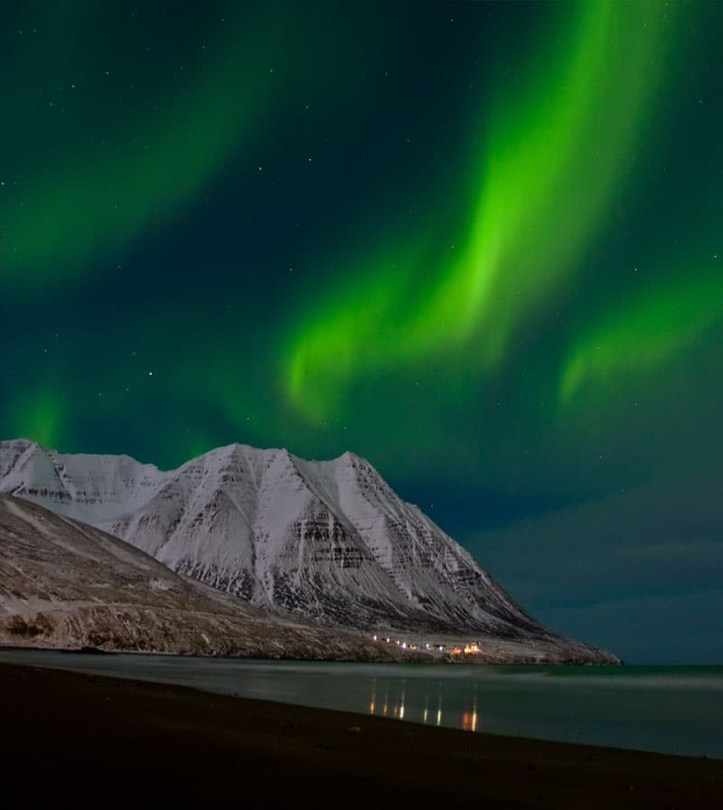 Snowy  mountain across a bay with dancing Northern Lights